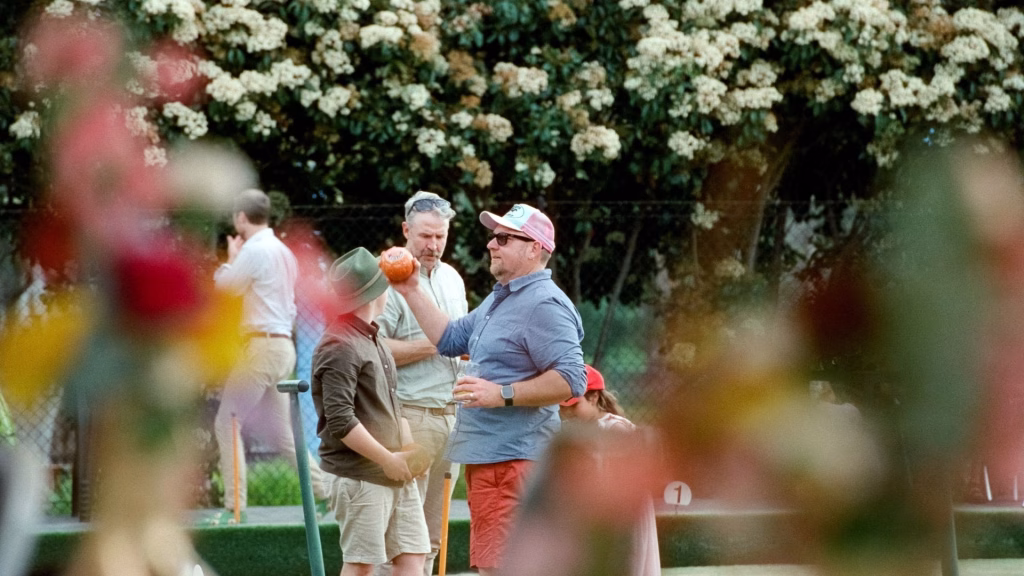 Candid color film image of wedding guests enjoying drinks and playing lawn bowls at the Adelaide Bowling Club during a sun-drenched afternoon session.