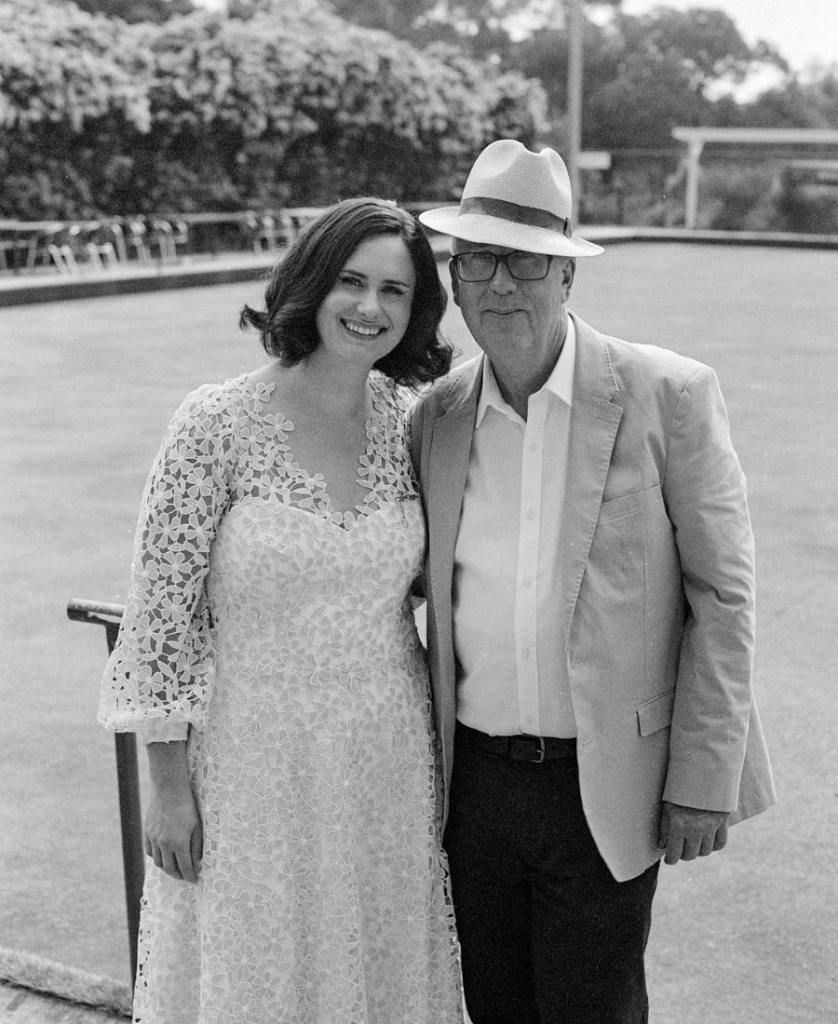A timeless black and white film photograph of a bride and her father sharing a tender moment at the Adelaide Bowling Club; featuring rich silvery tones, deep contrast, and authentic 35mm grain by Phoebe Kate Photography.