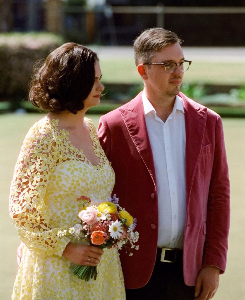 A romantic color film photograph of a bride and groom embracing on the Adelaide Bowling Club lawns; featuring warm, painterly tones, soft-focus greenery, and the iconic organic grain of 35mm film by Phoebe Kate Photography.