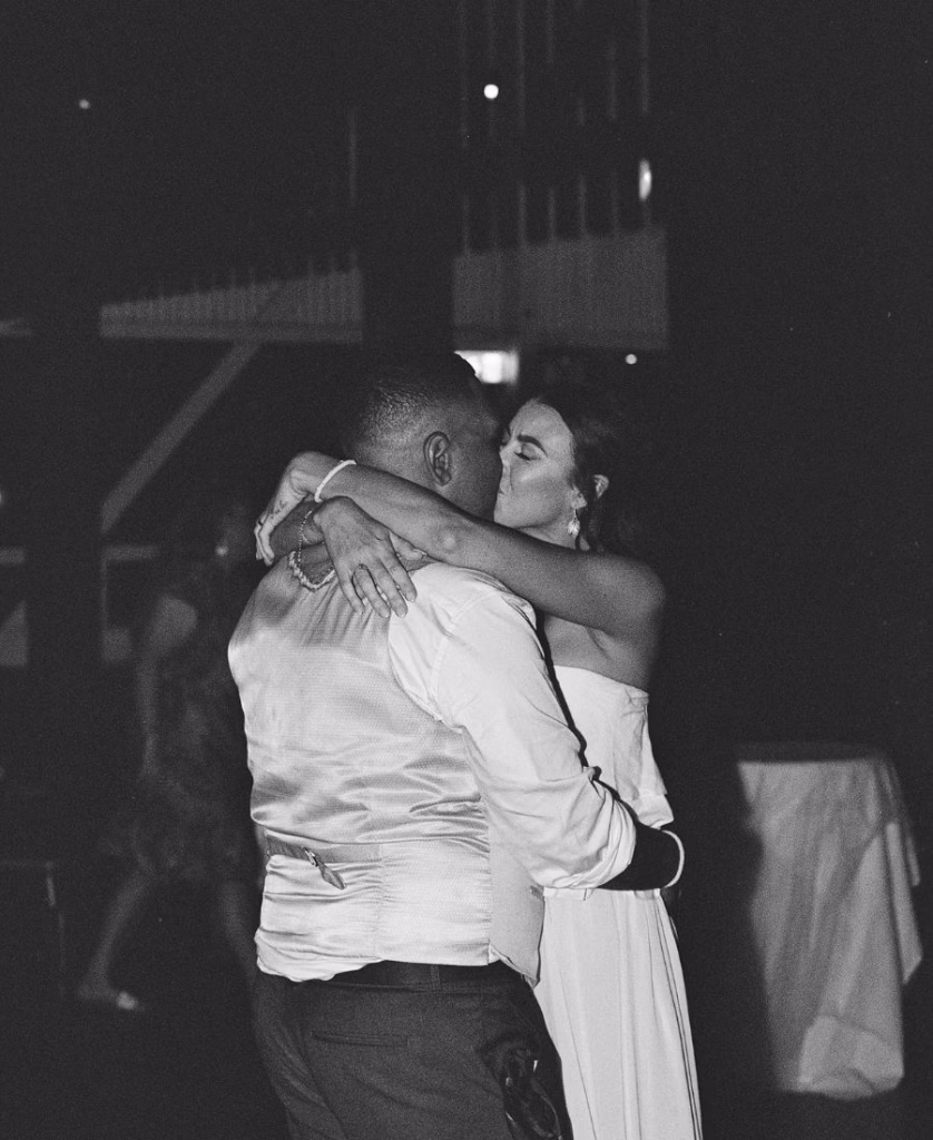 A romantic black and white film photograph of a bride and groom kissing in Cairns, North Queensland; featuring deep contrast, rich silvery tones, and a lush tropical backdrop captured on 35mm film by Phoebe Kate Photography.