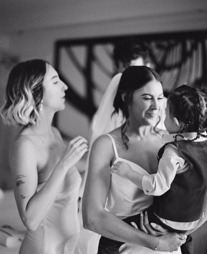 A tender black and white film photograph of a bride holding her toddler during the wedding day; a raw and emotional family memory by Phoebe Kate Photography.