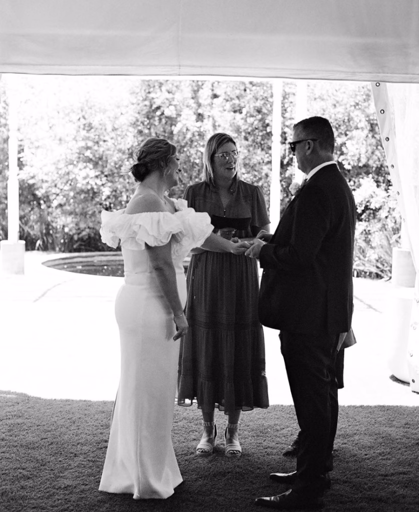 A candid wedding ceremony photograph of a couple standing with their celebrant during the exchange of rings; captured in a timeless, unhurried film style by Phoebe Kate Photography.
