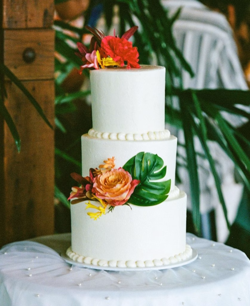 A detailed color film photograph of a three-layered tropical wedding cake at Riverlea Estate, featuring elegant floral styling and natural textures.