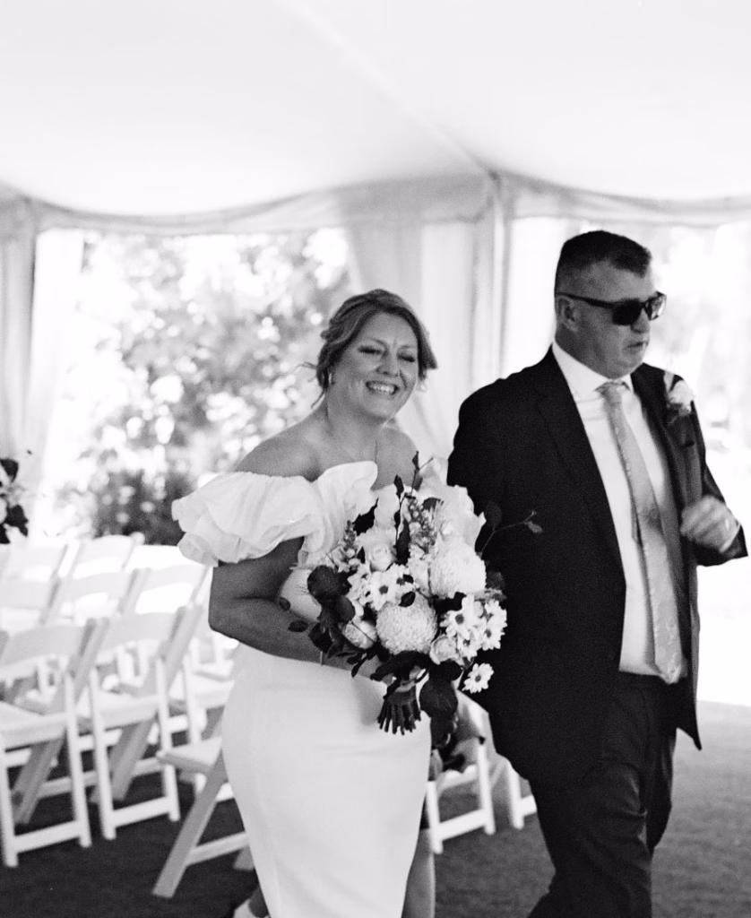 A classic black and white film photo of a newly married couple walking down the aisle, captured with a nostalgic, unhurried aesthetic and deep contrast by Phoebe Kate Photography.