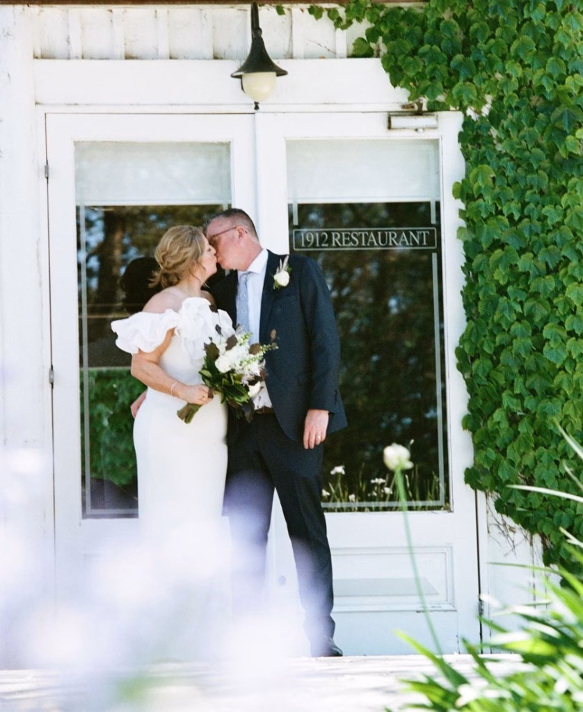 A joyful 35mm film photograph of a newly married couple's first kiss after their ceremony; featuring soft natural light and a nostalgic, unhurried aesthetic by Phoebe Kate Photography.