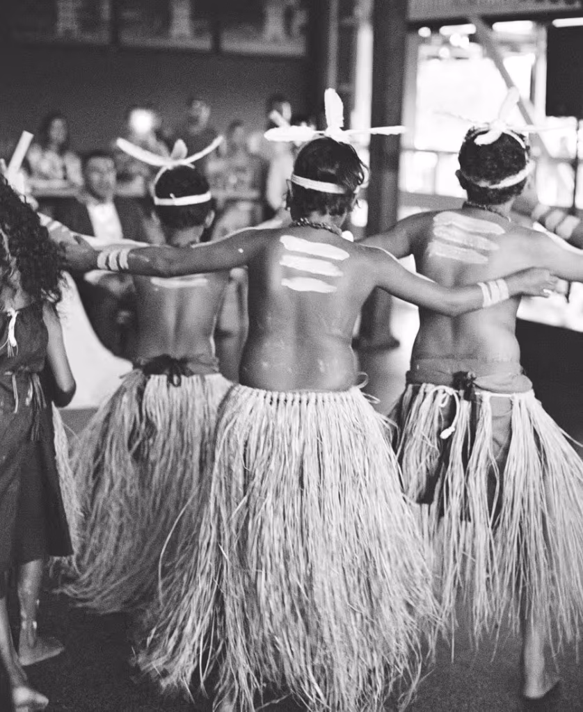 A striking black and white film photograph of Torres Strait Islander dancers in mid-performance, featuring rich contrast and cinematic movement.